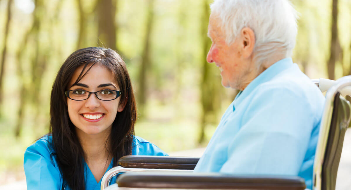 a younger woman in glasses smiling next to the older man on a wheelchair